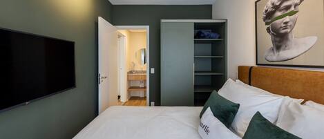 A bedroom with a bed, a television, a wardrobe, and a painting on the wall.