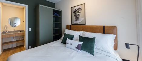 Una cama bien hecha con ropa de cama blanca y verde, un cabecero de madera y un almohadón con el nombre 'Charlie'.