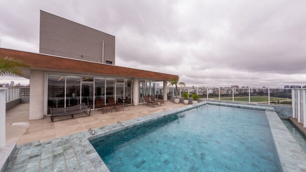 Una zona de piscina en la azotea con un edificio moderno, puertas de cristal y mobiliario exterior.