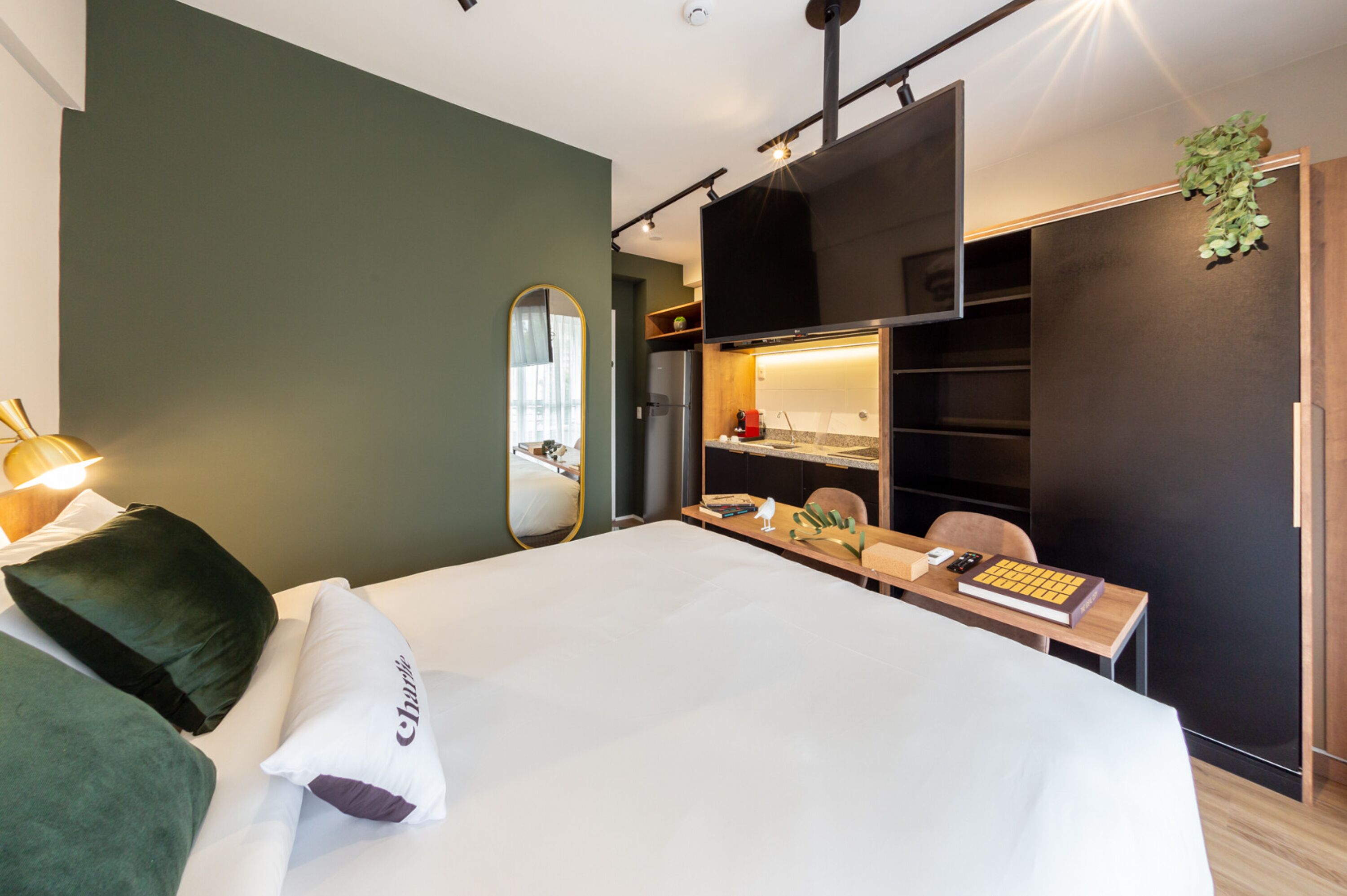 A modern hotel room with a large bed, a desk with a computer, a chair, and a wardrobe.