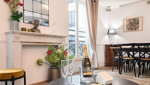 Un coin repas avec une table dressée pour deux personnes, une bouteille de champagne, deux verres et une assiette de macarons.