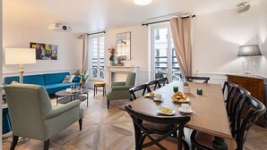 Un espace repas comprenant une table en bois, des chaises et une vue sur la ville grâce à de grandes fenêtres.