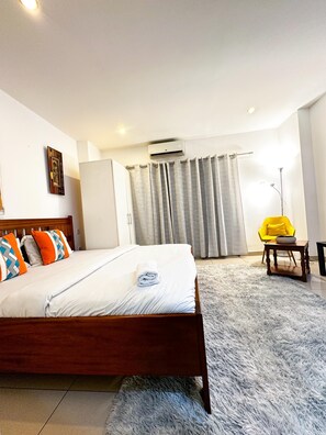 Un dormitorio con cama, una silla, una mesa y una ventana con cortinas.
