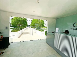 Zona de recepción con puerta de vidrio que da a un patio con árboles y un edificio al fondo.