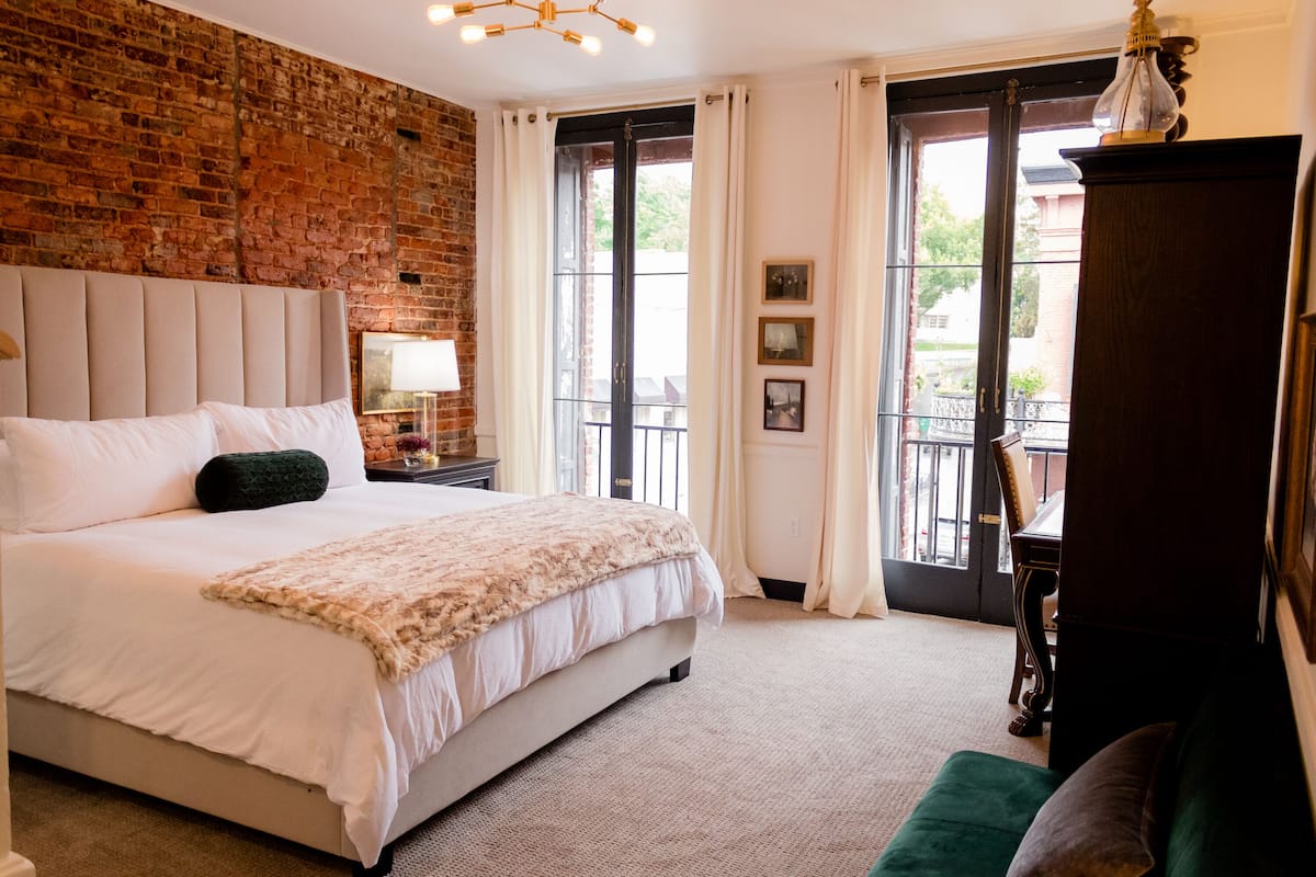 Quarto com uma cama grande, parede de tijolos, janela com cortinas e vista para o exterior.