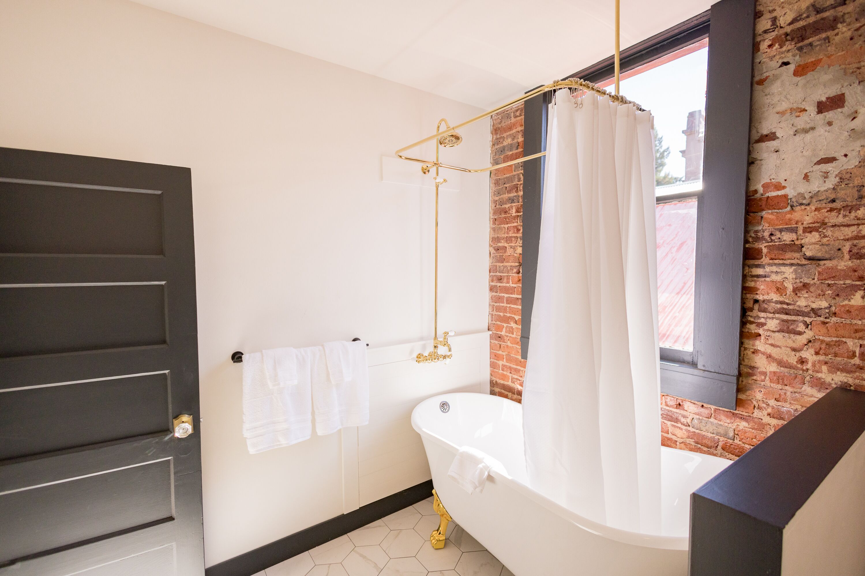 A bathroom with a white bathtub, a gold showerhead, and a brick wall.