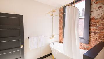 A bathroom with a white bathtub, a gold showerhead, and a brick wall.