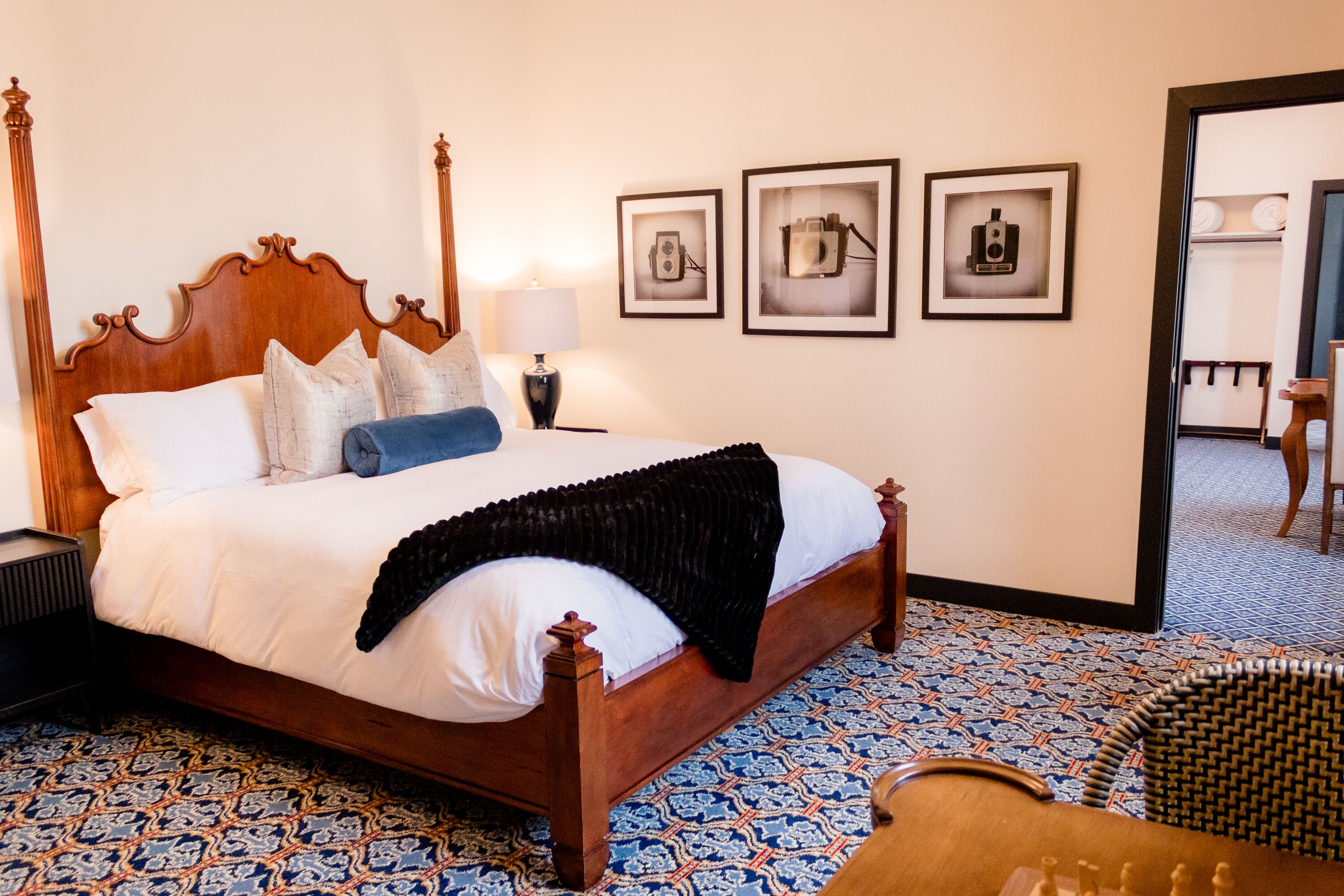 Una cama bien hecha con cabecera de madera, suelo estampado y tres cuadros colgados en la pared.