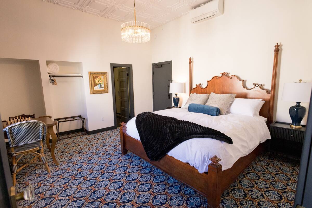 Quarto com cama grande, um lustre, cabeceira de madeira, piso estampado e uma cadeira.
