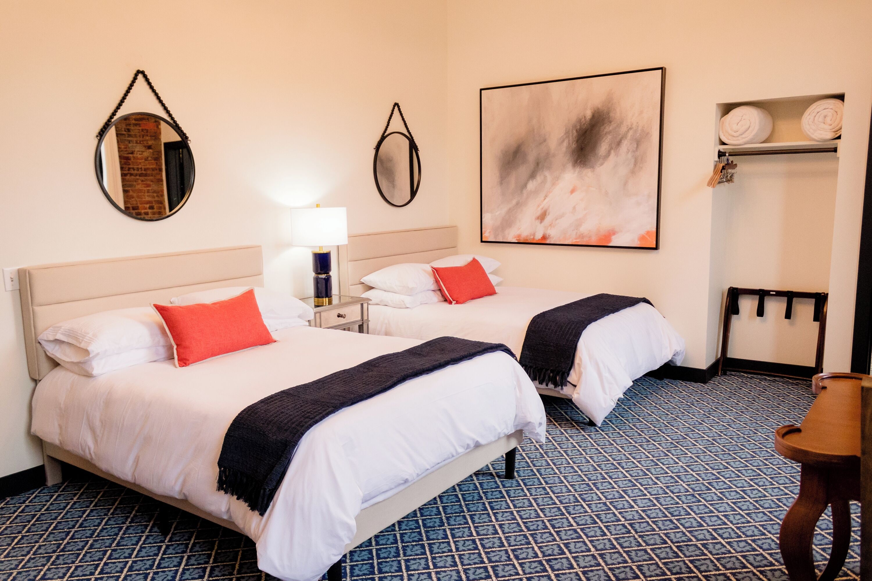 Une chambre d’hôtel avec deux lits, une table de chevet, une lampe, un miroir et un tableau au mur.