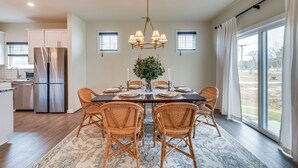 Uma sala de jantar com uma mesa grande, cadeiras de vime, um candelabro e vista para o exterior.