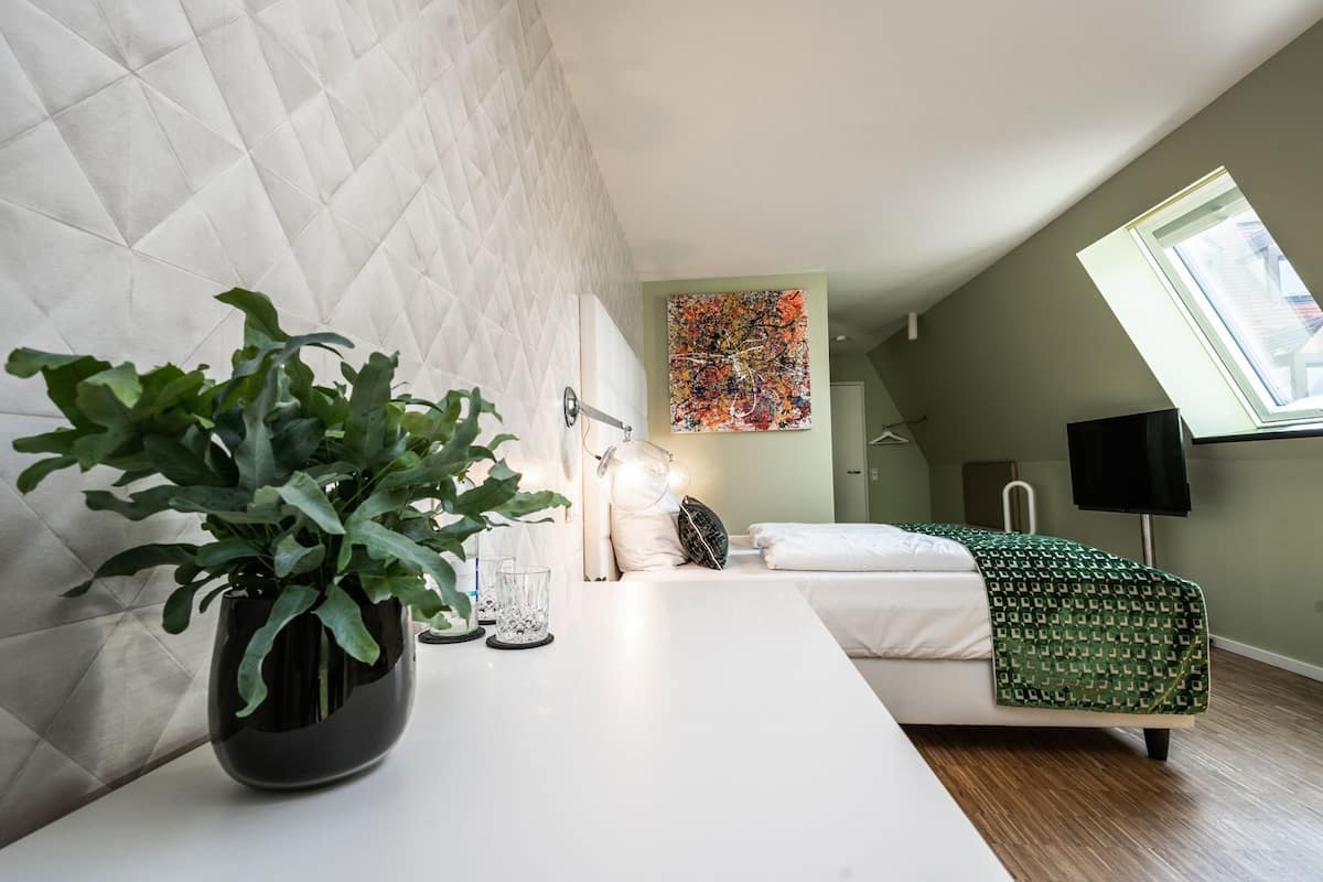 A modern bedroom with a bed, bedside table, potted plant, and a large window.