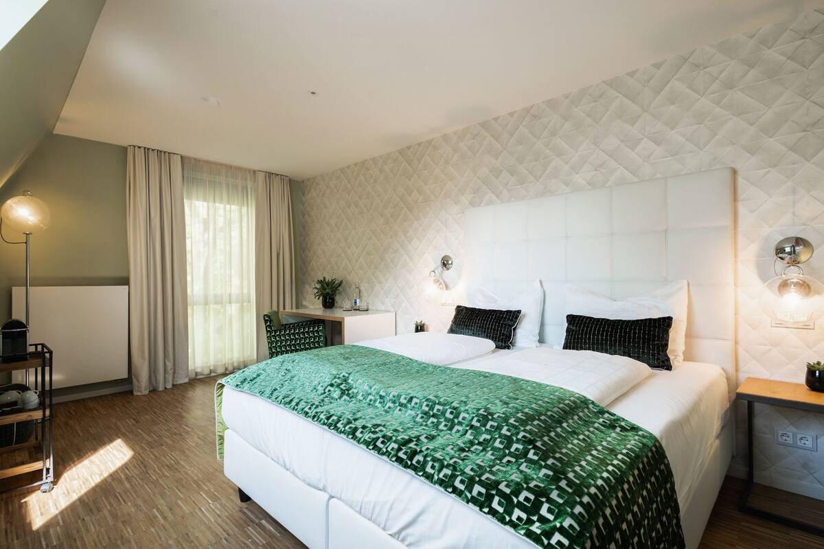 A modern hotel room with a large bed, a desk, a chair, and a lamp.