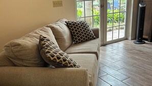 Un canapé beige agrémenté de coussins à motifs, un panier en fil de fer noir et un tableau accroché au mur.