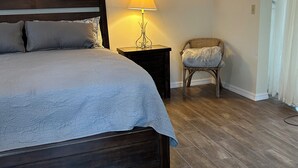 Une chambre à coucher avec un grand lit, une table de chevet avec une lampe, un fauteuil en osier et un tableau accroché au mur.