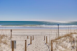 Une plage de sable bordée de barrières en bois, offrant une vue dégagée sur l’océan.