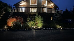 Une maison en bois à deux étages, dotée d’un balcon et entourée de rochers et de végétation.