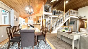 Un vaste espace de vie comprenant une table à manger pour quatre personnes, un escalier menant à l’étage supérieur et un coin salon confortable avec un canapé et des fauteuils.