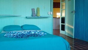 Een kamer met een bed, een plank met decoratieve objecten en een deur naar een andere kamer.