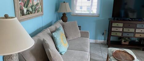 Un salon avec un canapé, une lampe, un téléviseur et un meuble en bois.