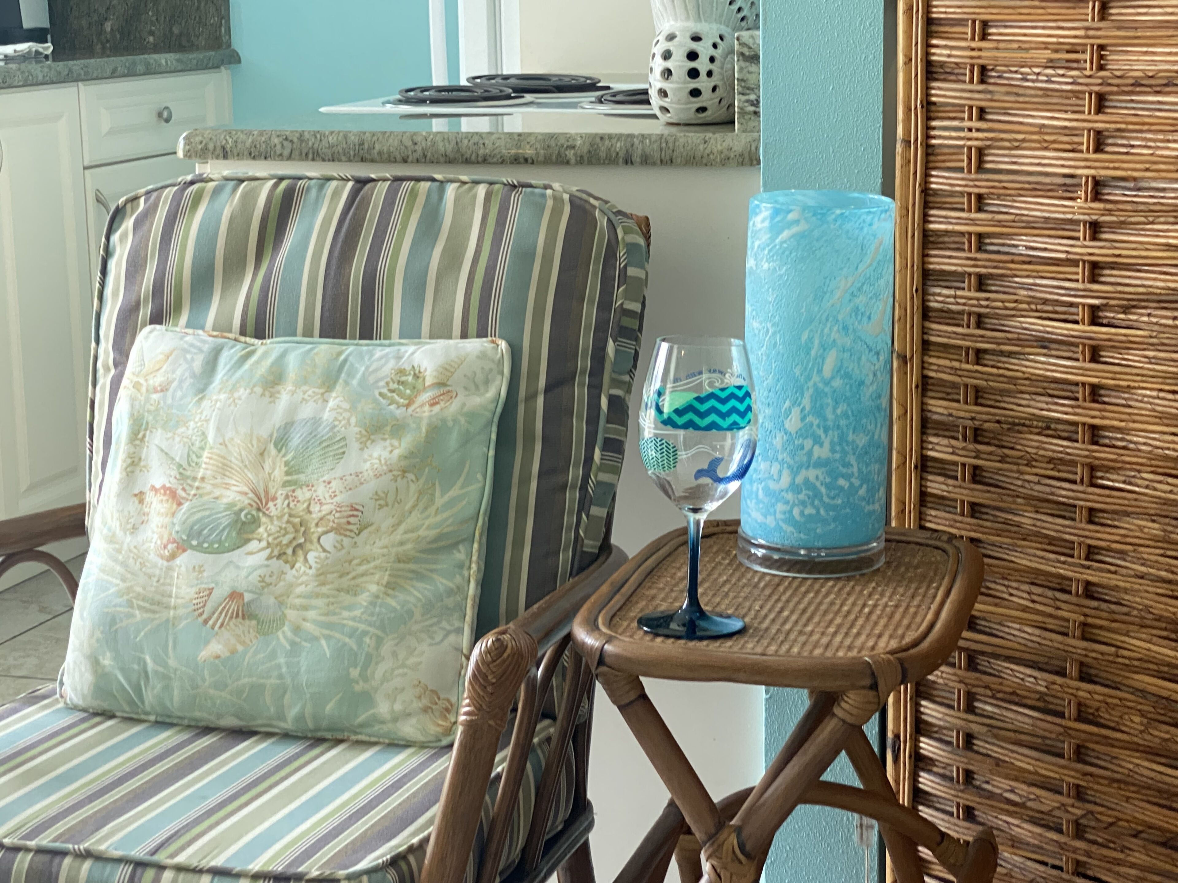 A wicker chair with a striped cushion and a glass vase with a blue pattern.