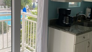 A kitchen with a coffee maker, a sink, and a view of a pool and palm trees through a balcony door.
