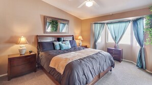 A bedroom with a bed, two bedside tables with lamps, a ceiling fan, and a window with curtains. - Cozy Lake Havasu City Home - Pool and Hot Tub (Lake Havasu City)