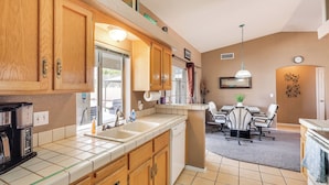A kitchen with wooden cabinets, a coffee maker, and a dishwasher. There is a dining area with a table and chairs. - Cozy Lake Havasu City Home - Pool and Hot Tub (Lake Havasu City)