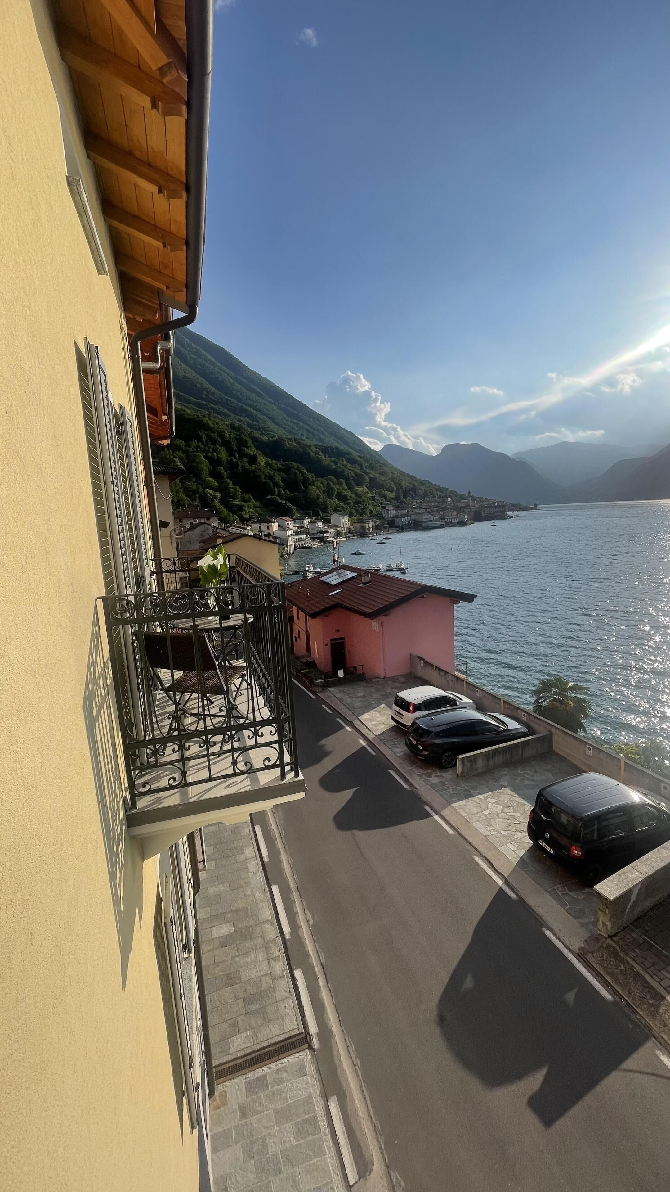 A balcony with a view of a coastal road, parked cars, and a pink building.