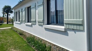 Un bâtiment doté de nombreuses fenêtres, de volets, d’une pelouse bien entretenue et d’un mur en pierre.