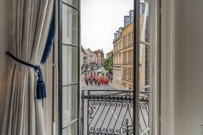 A view from a balcony with a wrought iron railing, overlooking a street with buildings and a group of people in red uniforms. - A central spot to explore Windsor in a beautiful, well-appointed apartment.  (Windsor)