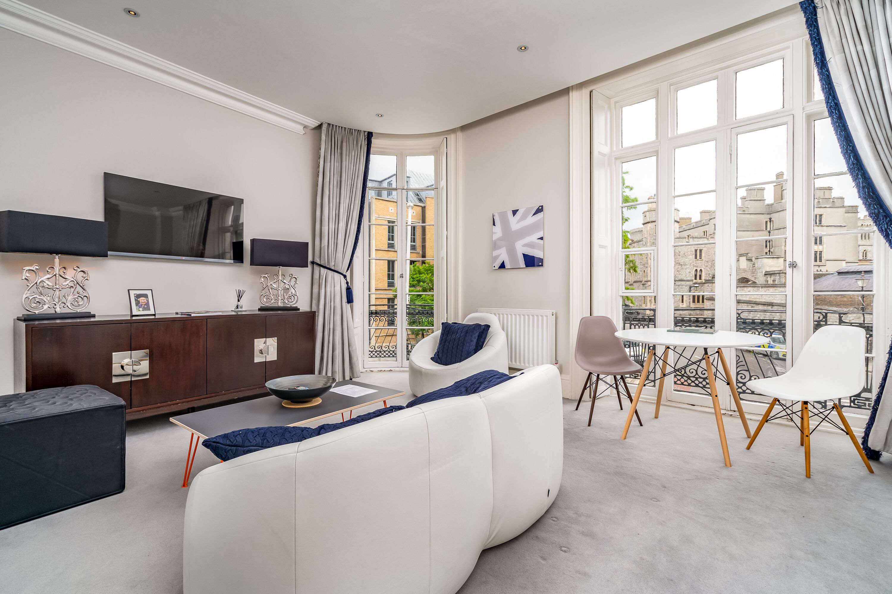 Una sala de estar moderna con un sofá blanco, un televisor de pantalla plana, un mueble de madera y vistas de la ciudad a través de grandes ventanales.
