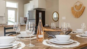 Une table à manger dressée avec de l’assiette blanche, des bols et des verres à vin, et une bouteille de vin placée au centre.