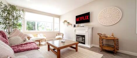 Una sala de estar con un sofá, una mesa de centro y una chimenea. Un televisor montado en la pared muestra 'NETFLIX'.
