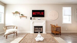 Un salon avec une cheminée, un canapé blanc, une statue de méditation, un logo Netflix et un élément de décoration murale de forme ronde.