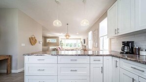Une cuisine moderne avec des meubles blancs, des plans de travail en granit et des luminaires suspendus.
