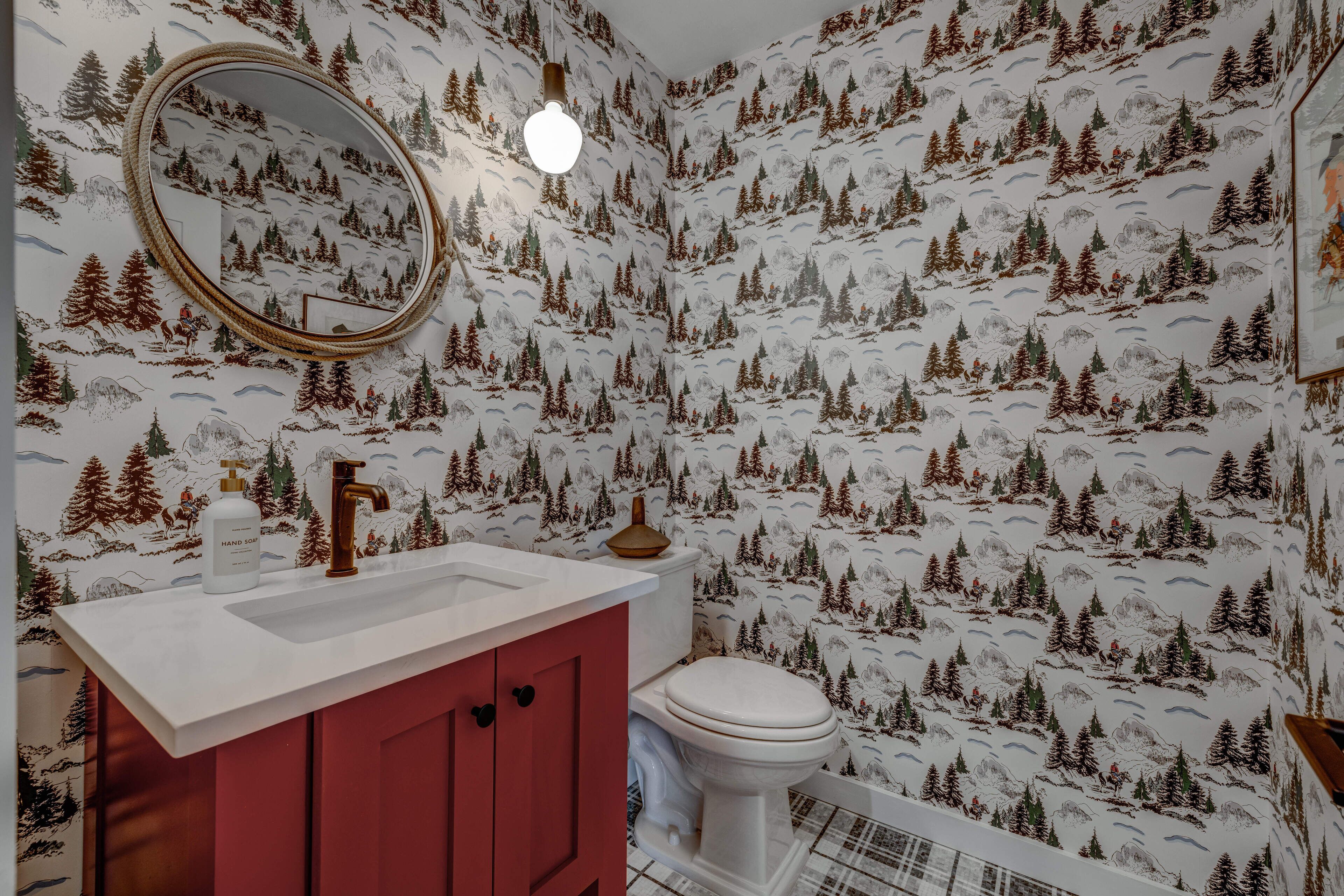 Ein Badezimmer mit einem weißen Waschbecken, roten Schränken, einer weißen Toilette und einem Spiegel mit rundem Rahmen.
