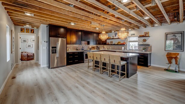 A spacious kitchen with a large island, dark cabinetry, and a wooden ceiling.