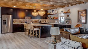 A modern kitchen with dark cabinets, a stainless steel refrigerator, wooden bar stools, and a central island.