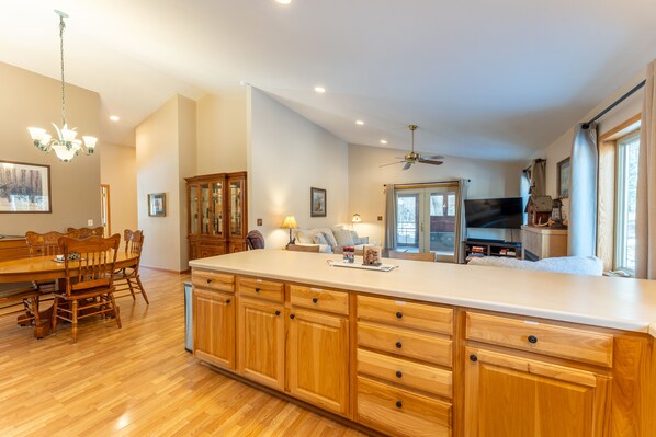 A spacious kitchen with wooden cabinets, a large island, and a dining area with a wooden table and chairs. - Wooded setting, close to town, clean! ATV & snowmobile from front door! (Ely)