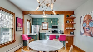 A modern kitchen with teal cabinets, a white countertop, and a central island. There is a dining area with a round table and chairs.