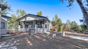 A two-story house with a covered porch, a fenced yard, and a driveway leading to a parked car. - Mtn Views + Playground: Family-Friendly Pine Cabin (Pine)
