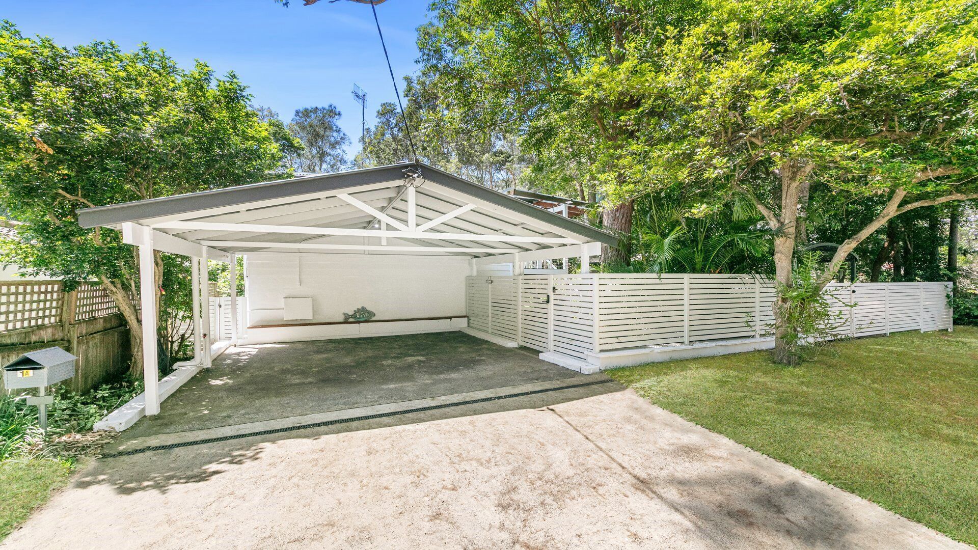 A covered garage with a concrete driveway, white exterior walls, and a fenced backyard.