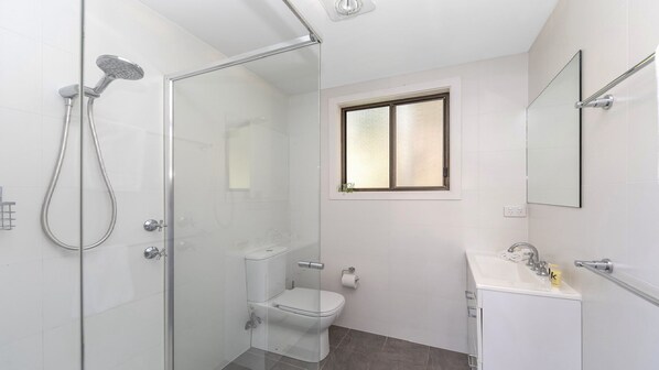 A modern bathroom with a glass-enclosed shower, a toilet, and a sink with a mirror. - Treetops on the Bay by HolidayCo. (HARDYS BAY)