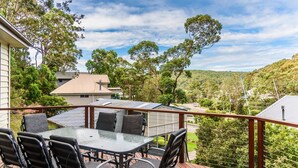 A deck with a glass-top table and chairs, overlooking a residential area with houses and trees.
