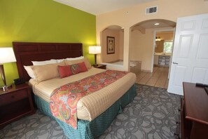 Habitación de hotel con una cama grande, una mesita de noche, una lámpara y vista al baño.