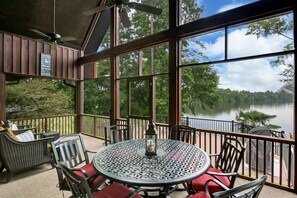 A covered outdoor seating area with a table and chairs, overlooking a lake.