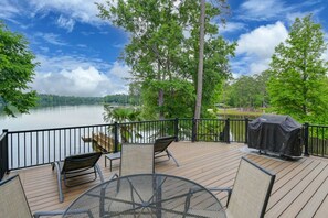 A deck with outdoor furniture, a grill, and a view of a lake surrounded by trees.
