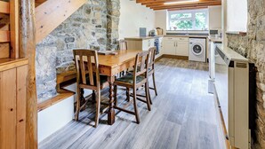 Een rustieke keuken met een stenen muur, houten balken en een eethoek met een houten tafel en stoelen.