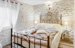 A bedroom with a stone wall, a metal bed frame, and two bedside lamps. - Cozy home in St Sauveur de Cruzière (St Sauveur de Cruzière)